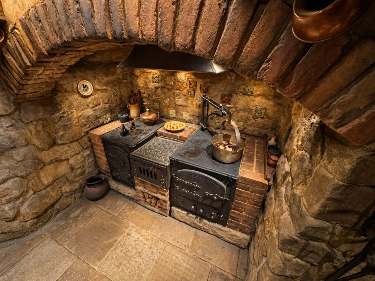 A Stone-And-Brick Kitchen Display With A Black Stove, Hanging Pots And Food Arranged On The Counters.