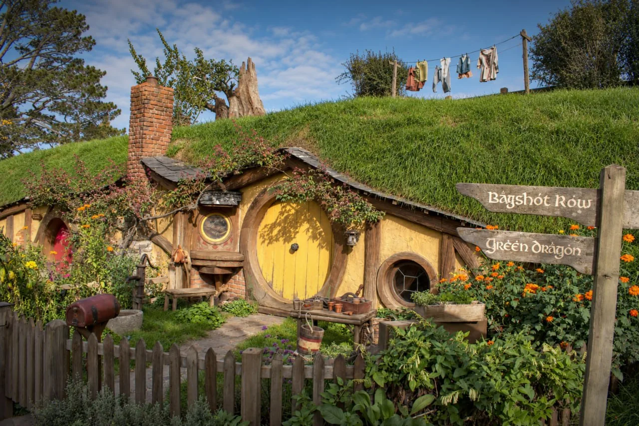 A Yellow Round Hobbit Door Beside A Garden And Laundry, With A Sign Pointing Toward Bagshot Row And The Green Dragon.