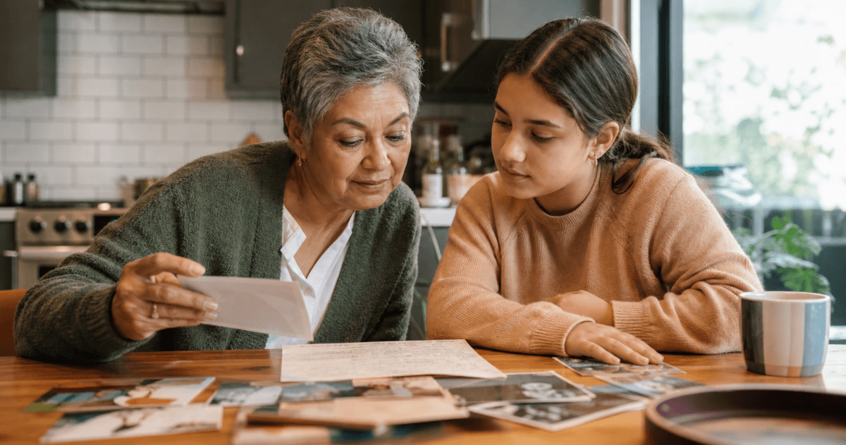 Pass Values To Grandchildren Featured Grandparent And Teenage Grandchild Looking Through Family Photos And A Handwritten Recipe Together